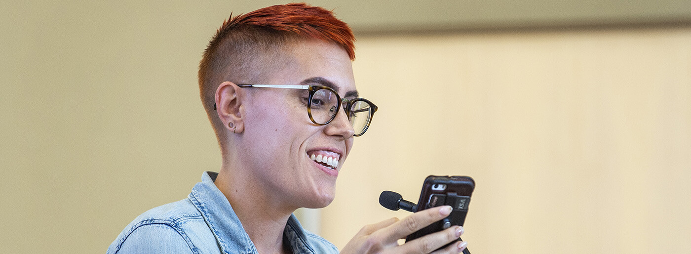 Student with short hair smiling and looking at a phone